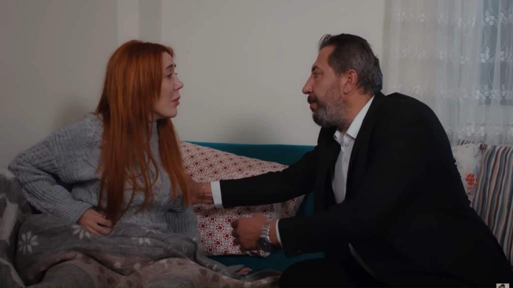 Yonca siedzi na kanapie. Tayyar dotyka jej ramienia, próbując uspokoić.