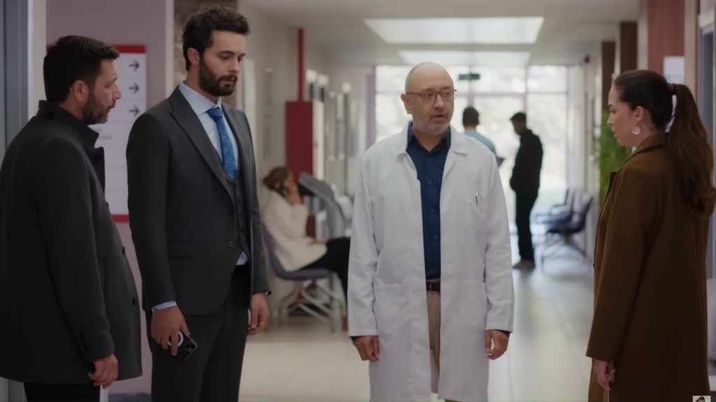 Nusret, Engin i Beyza rozmawiają z lekarzem na szpitalnym korytarzu.