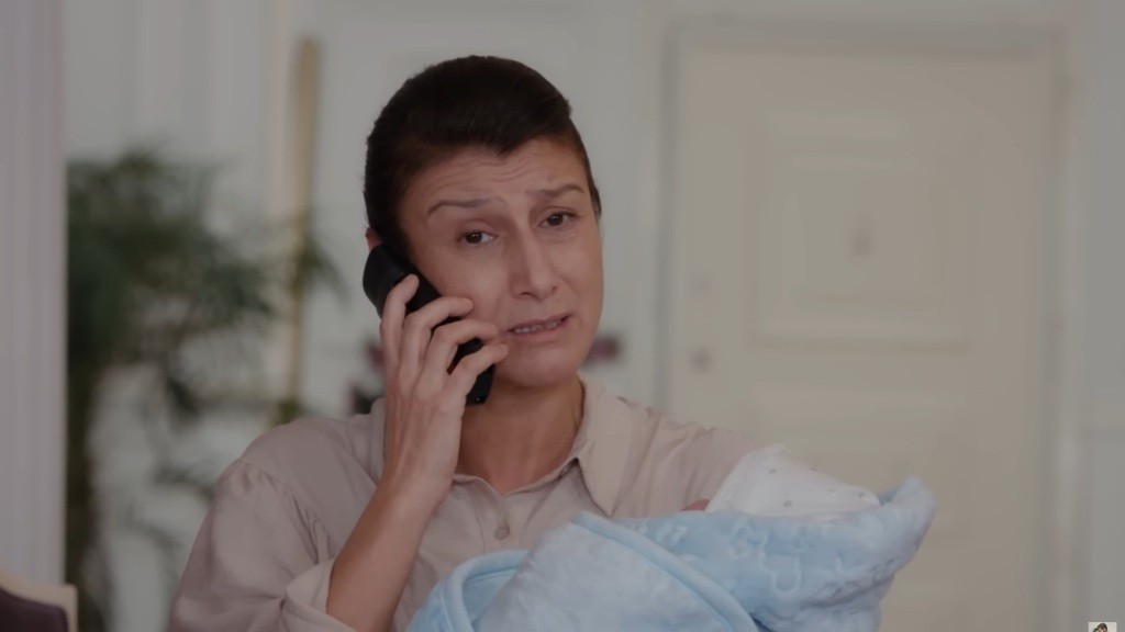 Fadime rozmawia przez telefon, trzymając na rękach niemowlę.