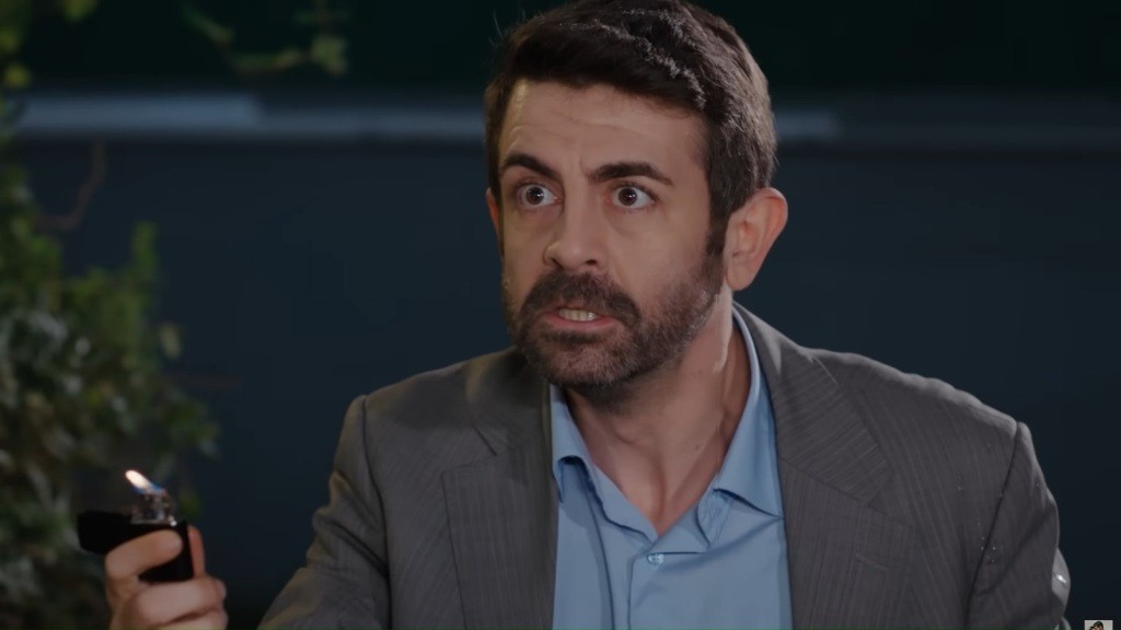 Cemil trzyma w ręku płonącą zapalniczkę i wygląda na zdenerwowanego.
