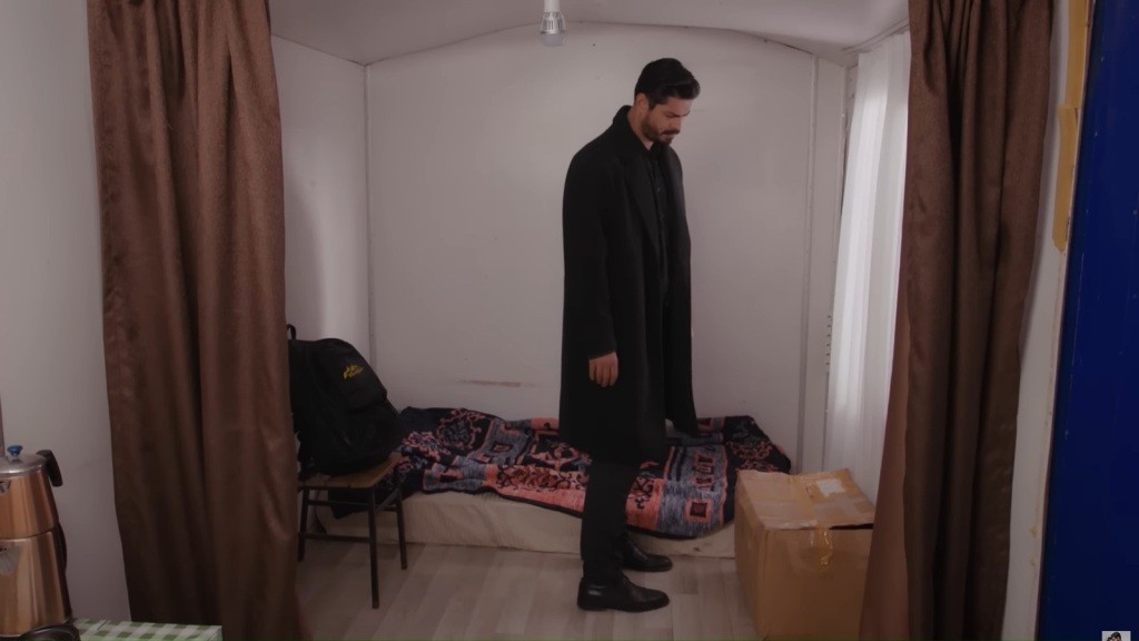 Cihan stoi w środku przyczepy i patrzy na leżące na podłodze pudełko.