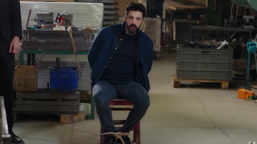 Magazyn. Melih siedzi przywiązany do krzesła.