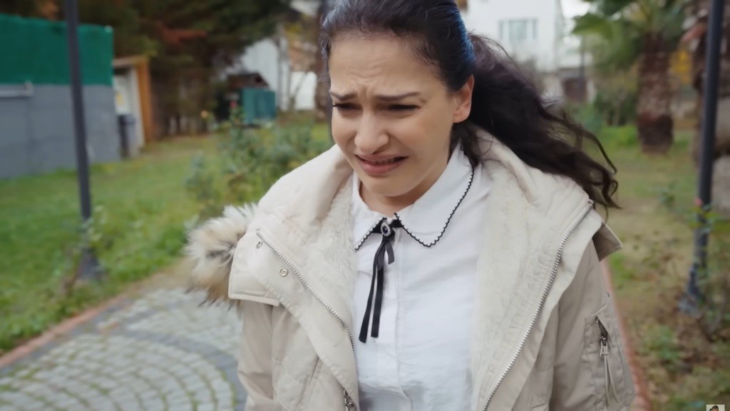 Gulsum płacze, stojąc na wysadzanej kostką alejce.