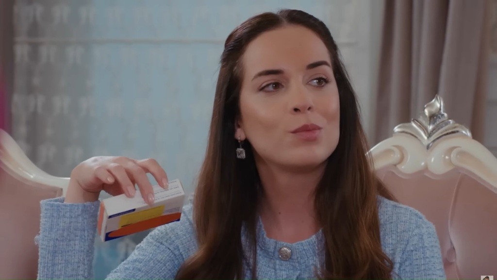 Beyza siedzi na ozdobnym fotelu i trzyma w rękach opakowanie po teście ciążowym.