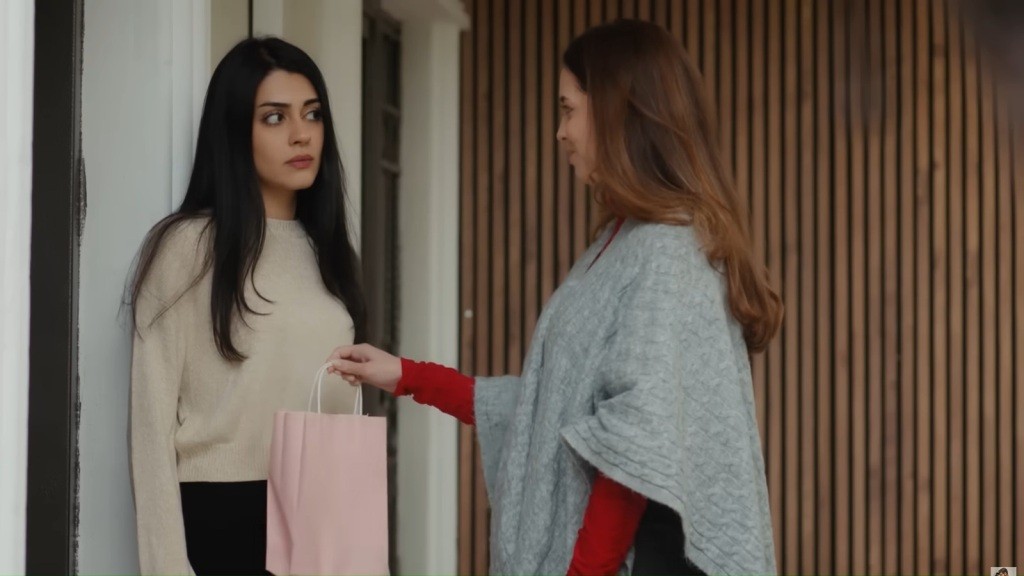 Beyza wręcza Hancer różową torebkę prezentową. Obie stoją przy drzwiach. Na twarzy Hancer maluje się wyraz napięcia.