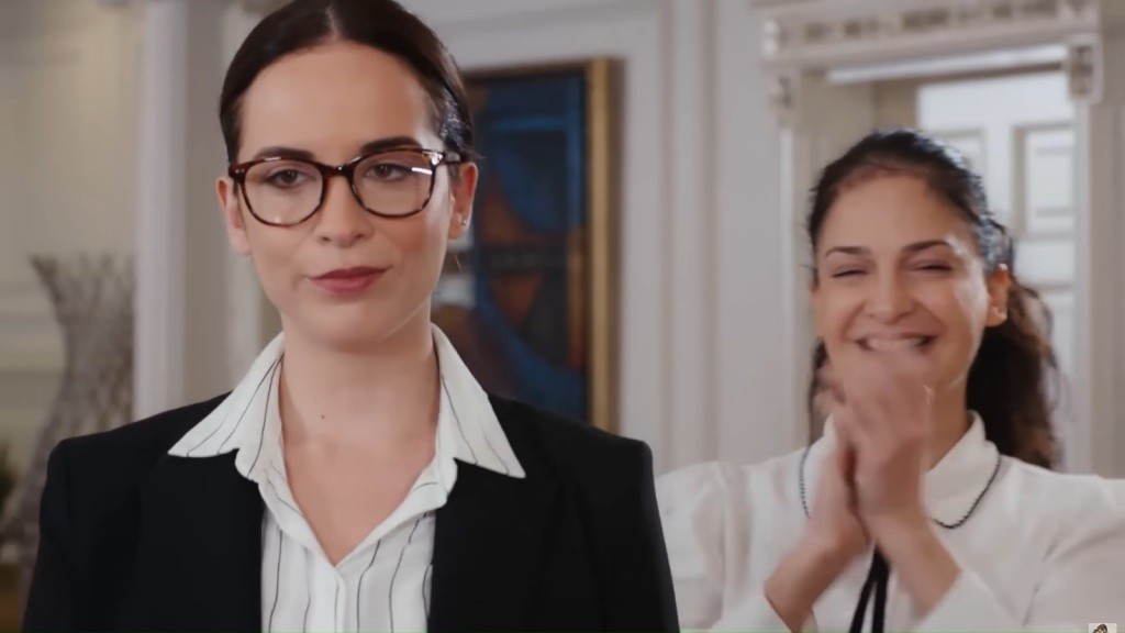 Profesjonalna kobieta w okularach stoi obok radosnej towarzyszki w jasnym salonie.