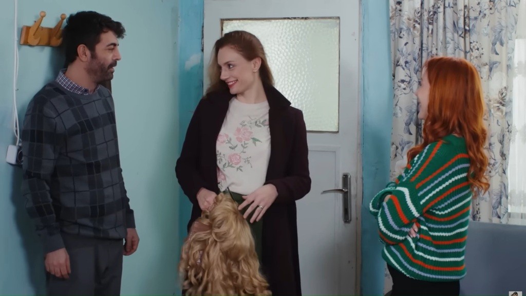 Trzy osoby rozmawiają w przedpokoju. Derya trzyma w rękach perukę, a Cemil i Yonca stoją obok niej.