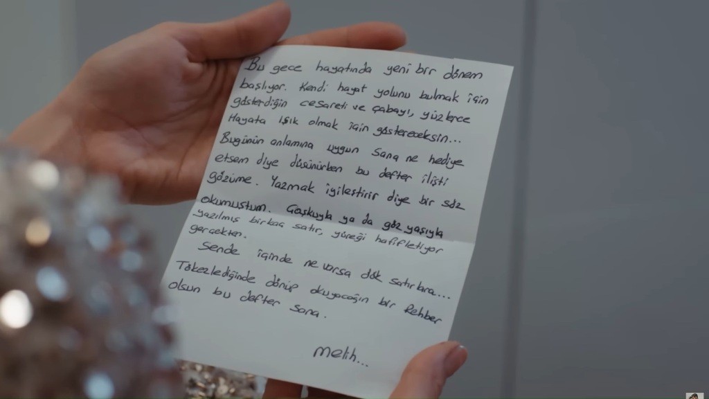 Zbliżenie na list w rękach Hancer, podpisany imieniem Meliha.