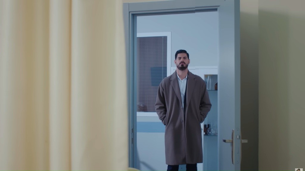 Cihan stoi w otwartych drzwiach sali szpitalnej.