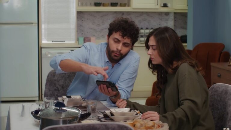 Engin i Sila siedzą przy stole i patrzą w ekran telefonu.