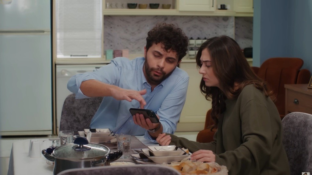 Engin i Sila siedzą przy stole i patrzą w ekran telefonu.