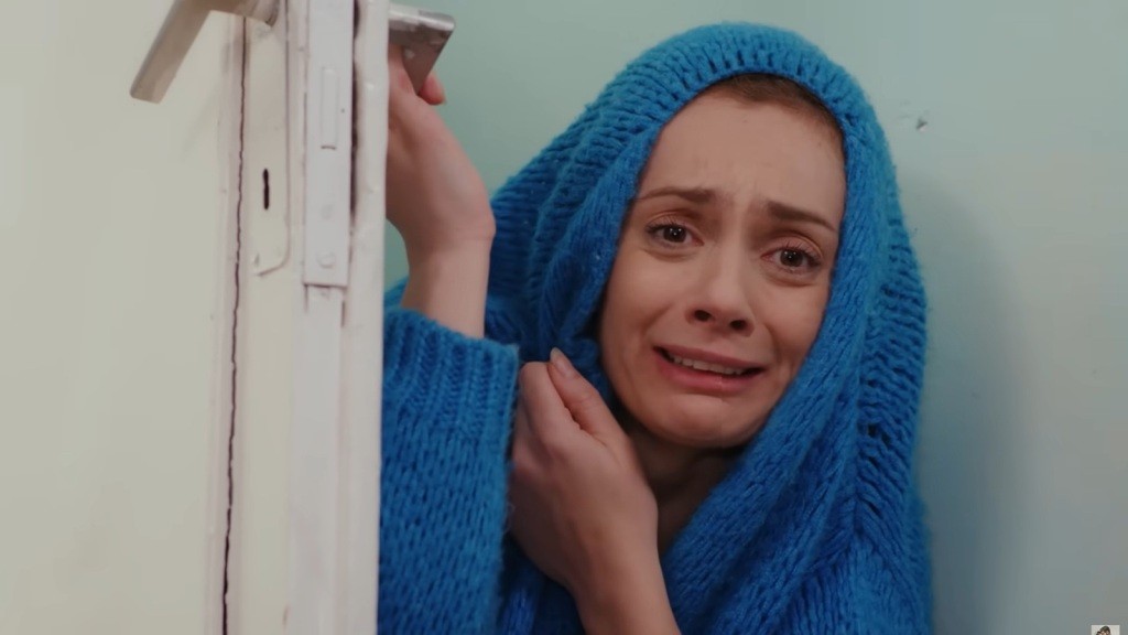 Derya chowa się za drzwiami. Na głowę ma naciągnięty niebieski sweter.
