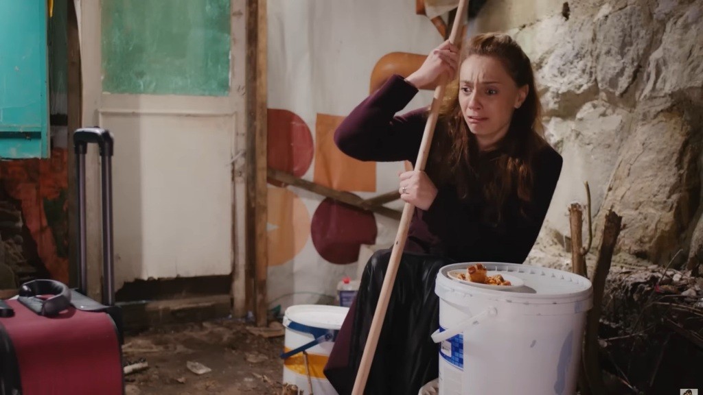 Derya znajduje się w obskurnym miejscu. W rękach ściska kij od szczotki. Przed sobą ma plastikowe wiadro, a na nim talerz z resztką menemenu.