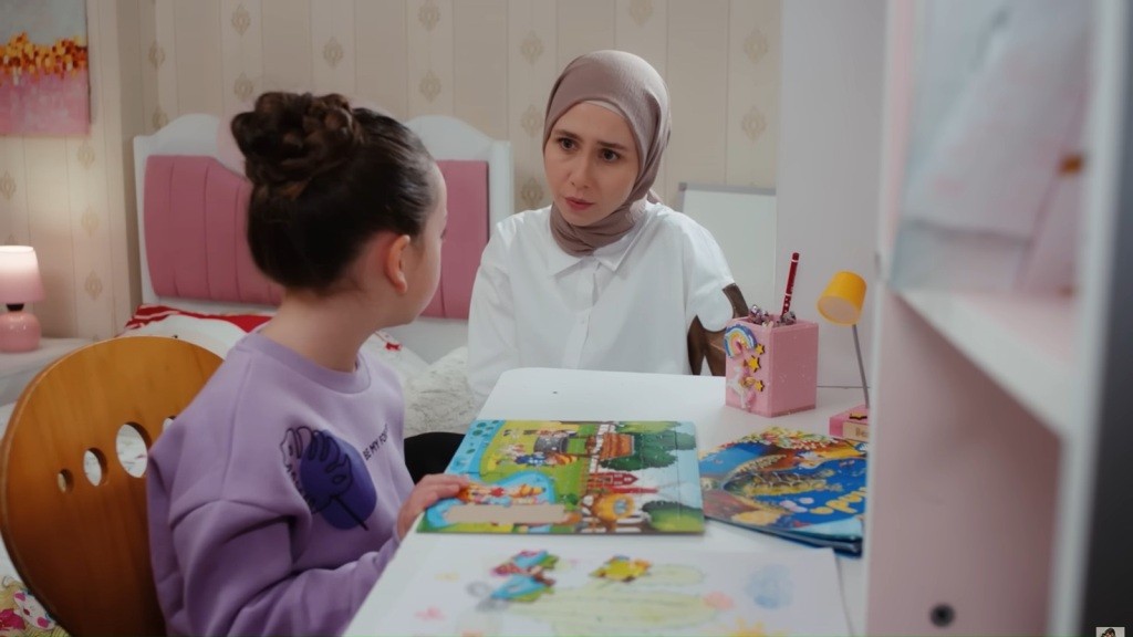 Mine siedzi przy biurku i układa puzzle. Obok niej siedzi Sinem.