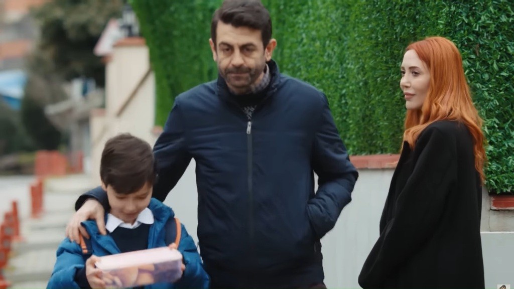 Emir trzyma w rękach pudełko z jedzeniem. Cemil idzie obok, obejmując go ramieniem. Yonca patrzy za nimi.