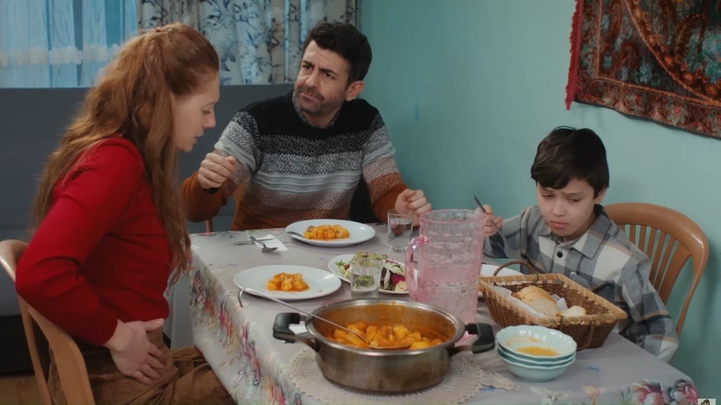Derya, Cemil i Emir siedzą przy stole. Chłopiec ma skwaszoną minę, a jego matka przykłada dłoń do brzucha.