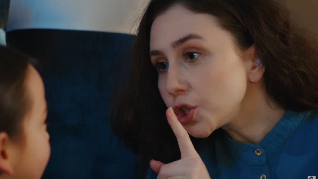 Sinem zbliża palec wskazujący do ust, pokazując Mine, by była cicho.