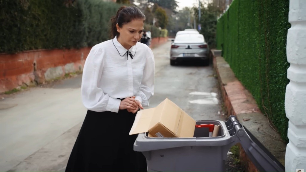 Gulsum stoi przy kontenerze na śmieci.
