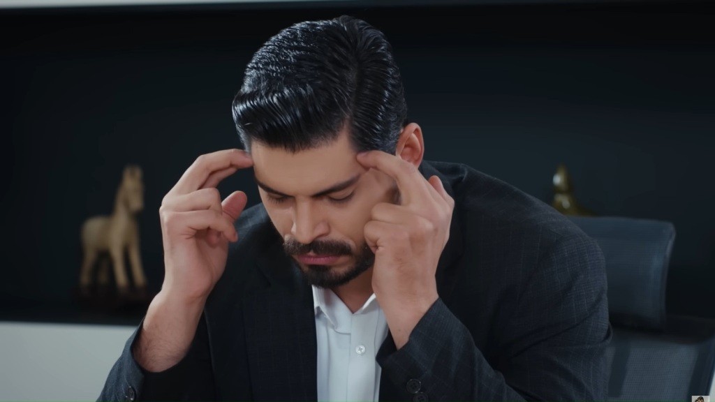Cihan siedzi w fotelu biurowym i masuje się po skroniach.