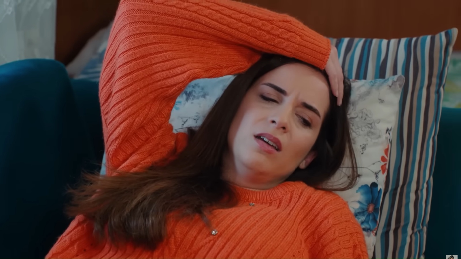 Beyza leży wyczerpana na kanapie po dniu ciężkiej pracy. Trzyma się ręką za głowę, co sugeruje dotkliwą migrenę.