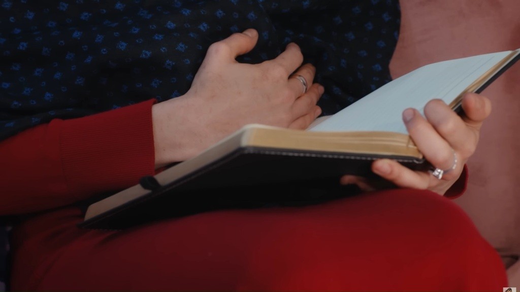Zbliżenie na pamiętnik oraz dłoń Hancer położoną na brzuchu.