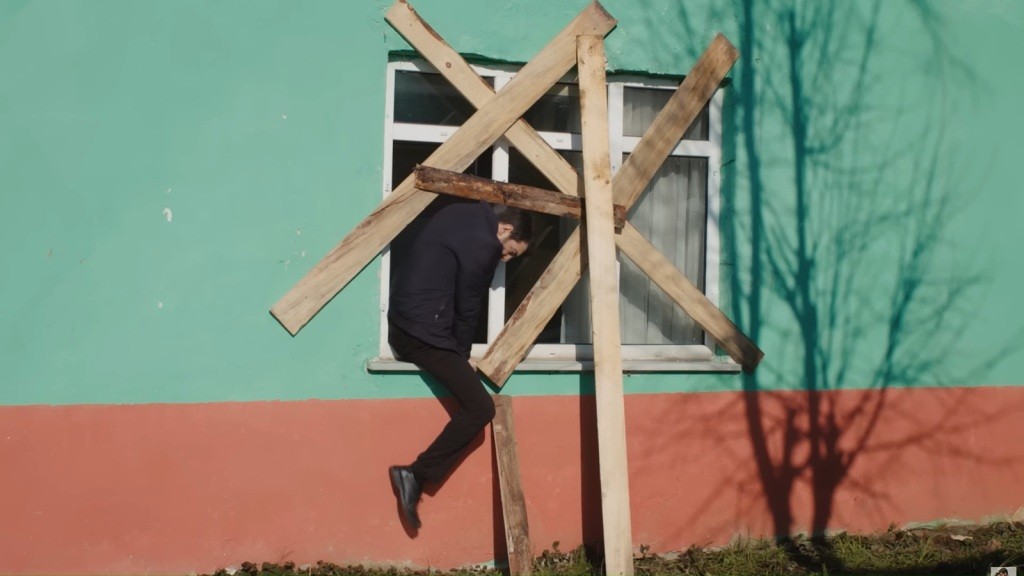Cemil przeciska się na zewnątrz przez zabite deskami okno.